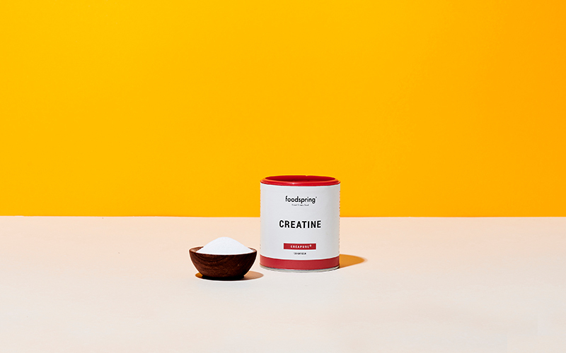 a canister of foodspring creatine powder in front of a mustard-yellow background